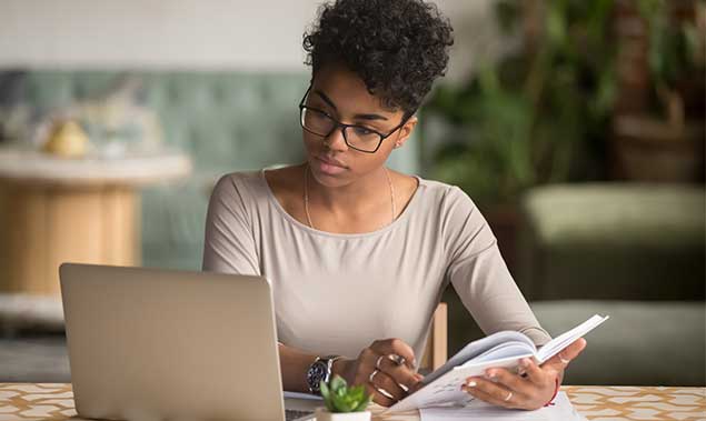 Focused Young African American Businesswoman Or Student Looking At Laptop Holding Book Learning