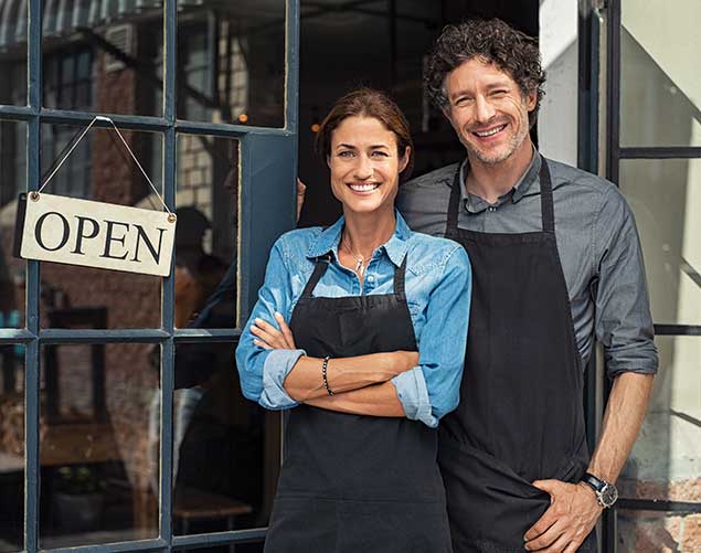 Two Cheerful Small Business Owners Smiling And Looking At Camera While Standing At Entrance Door